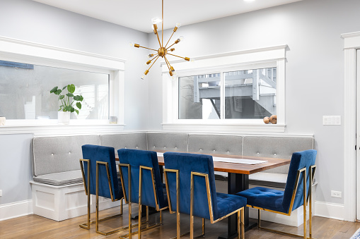 A modern, corner dining room with bench seating, a gold sputnik chandelier, blue chairs with gold legs surrounding a wooden table, and hardwood floors.