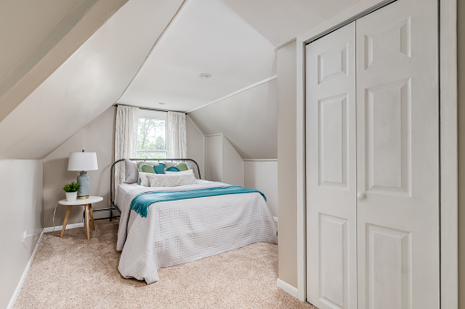 A cozy, slanted ceiling bedroom, a lamp on the nightstand beside the bed, and a large closet door.