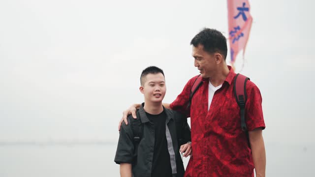 Asian Chinese down syndrome young man walking with father on wooden bridge Penang seaside during overcast morning