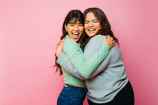 Excited women best friends having fun while laughing and hugging sharing love against a pink studio background