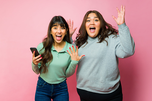 Excited women best friends celebrating screaming with happiness while texting on the smartphone