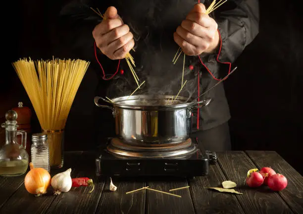 Professional chef prepares Italian pasta in a saucepan with vegetables. Close-up of cook hands while cooking in kitchen