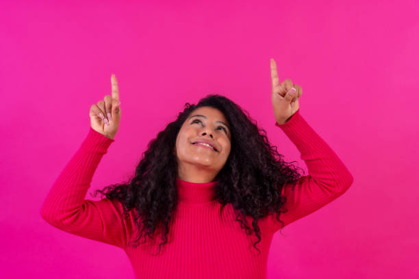 istock Curly-haired woman pointing up on a pink background, studio shot, copy paste 1458048381