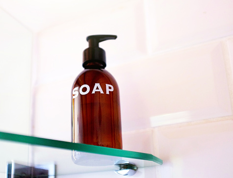 Guesthouse bathroom supplies stylish brown glass squirt bottle of plainly labeled soap, standing on a shelf in the shower.