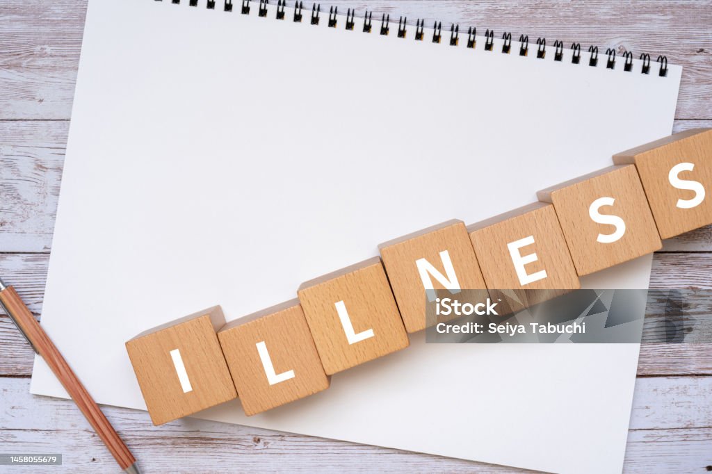 Wooden blocks with "ILLNESS" text of concept, a pen, and a notebook. Alphabet Stock Photo