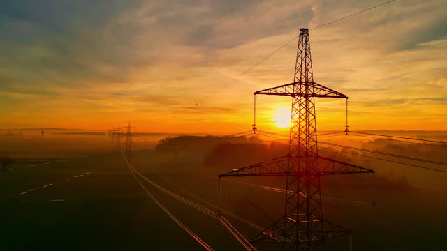 Electricity pylons and power lines against rural dramatic sunset sky