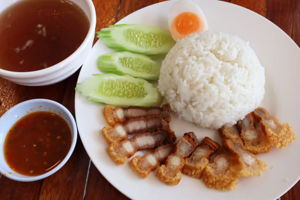 istock Thai-Style Fried Pork Belly served on rice with half boiled egg, sliced cucumber, soup and spicy sauce. 1458064023