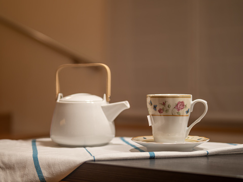 CUP OF TEA AND WHITE TEAPOT IN WARM KITCHEN. HOMELIKE. RELAXING MOMENT. SELECTIVE FOCUS.