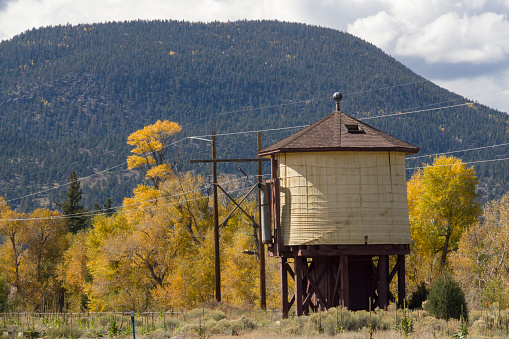 The 1881 built Denver and Rio Grande water tank stands near telephone poles in South Fork, Colorado with fall colors and the Rio Grande National Forest in the background.