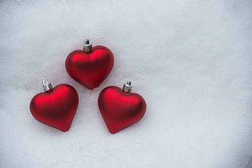 Three red heart shaped Christmas decorations on white snow, as symbol of love for Valentine's day celebration