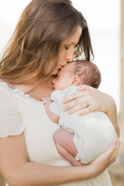 istock A Young Mother Holding Her Newborn Son Relaxed & Enjoying QualityTime Snuggling Her Boy While in a Stone Gazebo on the Water in a Relaxing Meditation Garden in Palm Beach, Florida for Lifestyle Newborn Family Photos 1458070884