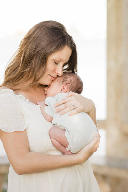 istock A Young Mother Holding Her Newborn Son Relaxed & Enjoying QualityTime Snuggling Her Boy While in a Stone Gazebo on the Water in a Relaxing Meditation Garden in Palm Beach, Florida for Lifestyle Newborn Family Photos 1458070886