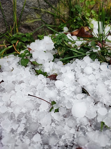 Hailstones in various sizes covering the ground next to a stone wall after a heavy hailstorm. Vertical abstract nature background