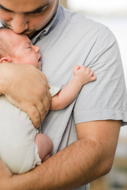 istock A Sweet Young Father Holding His Newborn Son While Standing Relaxed & Enjoying QualityTime Together in a Stone Gazebo on the Water in a Relaxing Meditation Garden in Palm Beach, Florida for Lifestyle Newborn Family Photos 1458073284