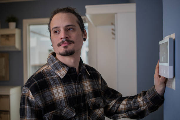 istock Young man adjusts the temperature at home with a device on the wall 1458076073
