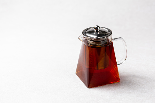 Glass teapot with hot black tea on white background