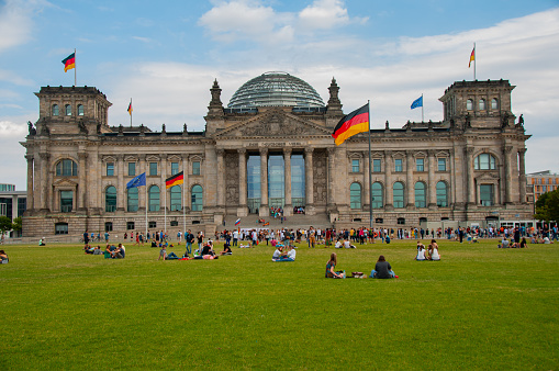 The Reichstag building in Berlin on a sunny day in the summer with a crowd of people on the grass and the German flag