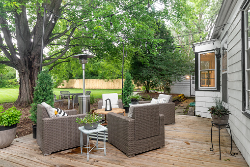Elmhurst, IL, USA - June 6, 2021: A cozy backyard patio of a white farmhouse with furniture, string lights, and wooden deck.