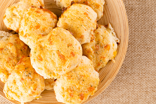 Fresh baked cheese biscuits close-up on a wooden plate, flat lay with copy space