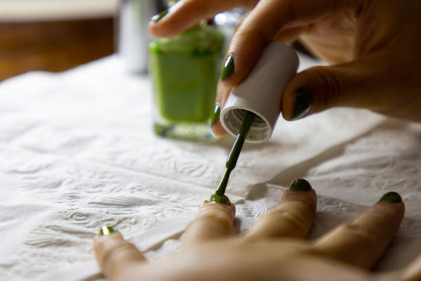 A woman applies nail polish to her fingernails.