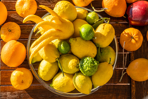 Various yellow and green type fresh ripe lemon fruits in a glass bowl. Group of organic lemons under sunny warm light with shallow depth of field. Pure antioxidant vitamin C. Natural food background with copy space.