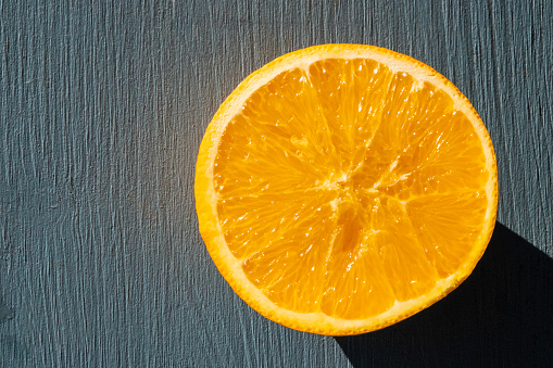 Circle pattern of a freshly cut yellow citrus fruit on blue wood table at sun light. Top view on food background with copy space.