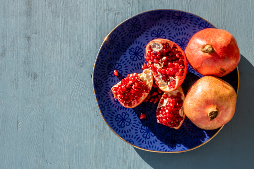 Fresh harvested full and halfed juicy pomegranate fruits on a blue decorated plate standing on wooden table. Top view on food background with copy space.