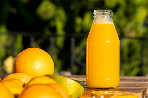 Various fresh ripe lemon fruits arranged arround a glass bottle with a yellow liquid citrus juice on wood table in the garden. Group of organic lemons under sunny warm light. Pure antioxidant vitamin C. Natural food background with copy space.