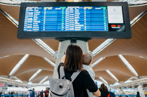 An Asian Chinese mother carrying her baby and looking at arrival departure board in airport