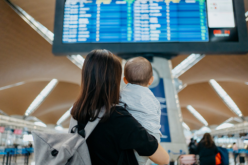 An Asian Chinese mother carrying her baby and looking at arrival departure board in airport