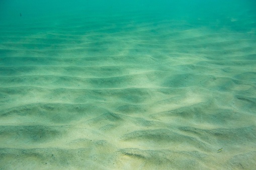 Sand ripples under water with sunlight and aqua sea