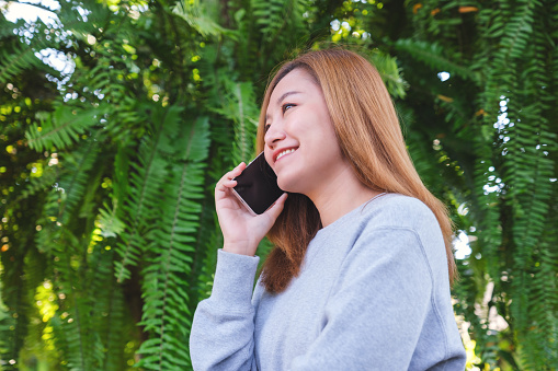Portrait image of a beautiful young asian woman holding and talking on mobile phone in the outdoors