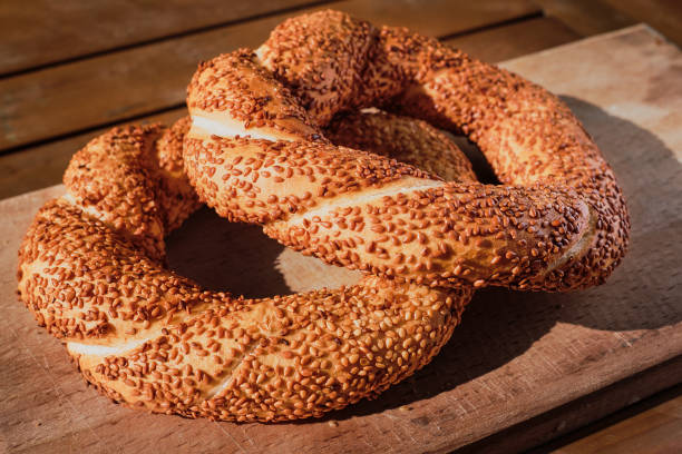 bagel recém-assado com sementes de gergelim em uma mesa de madeira aos raios de sol. pão turco simit close-up, doces frescos para o café da manhã. - simit - fotografias e filmes do acervo