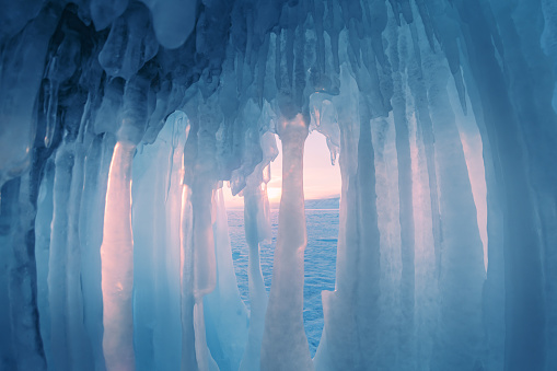 Ice cave with icicles on Baikal lake at sunset. Winter landscape of Baikal lake, Siberia, Russia