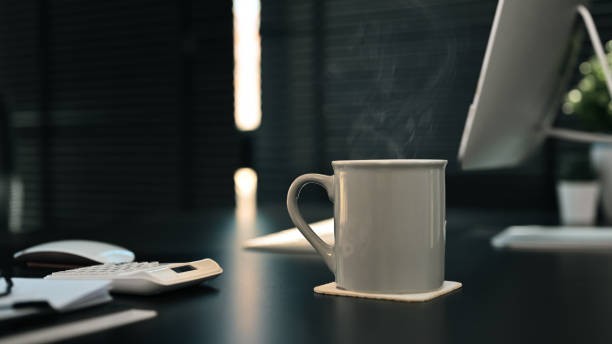 Cup of hot coffee on black wooden table with computer, document and calculator on background. Relaxing moment concept.