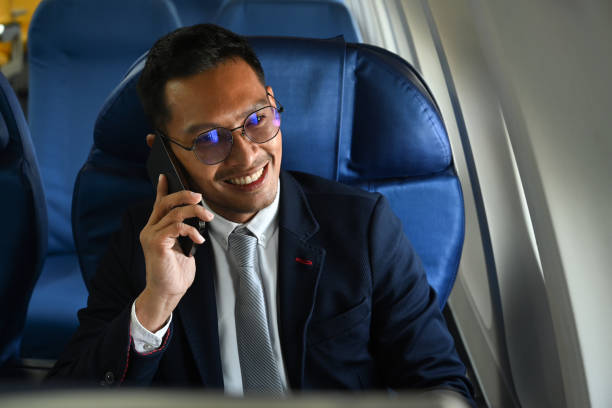 istock Successful businessman in suit talking on mobile phone while sitting comfortable seat in airplane cabin. 1458125961