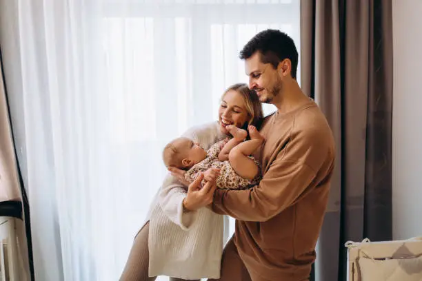 The young cheerful heterosexual couple joy of their baby girl at home. New life. Love emotion. Care about baby