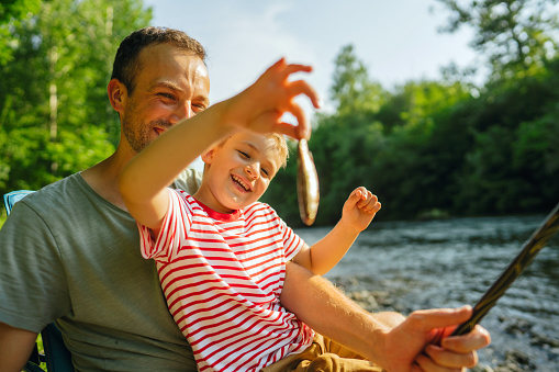 Photo of a little boy and his father spending quality time together while fishing on the riverbank