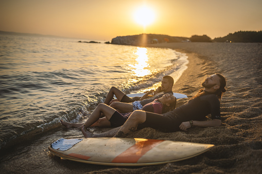 Group of young surfers resting on the beach at sunset, after their surf ride.