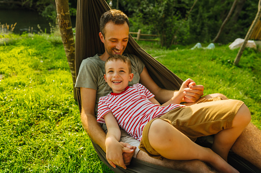 Cute little blond caucasian boy relaxing and having fun in multicolored hammock in backyard or outdoor playground. Summer active leisure for kids. Child swinging on hammock. Activities for children