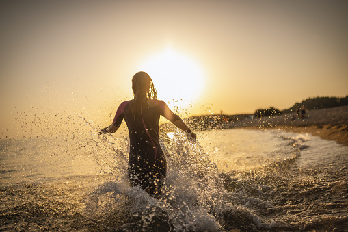 Photo of female surfers running into the water at sunset with surfboards .