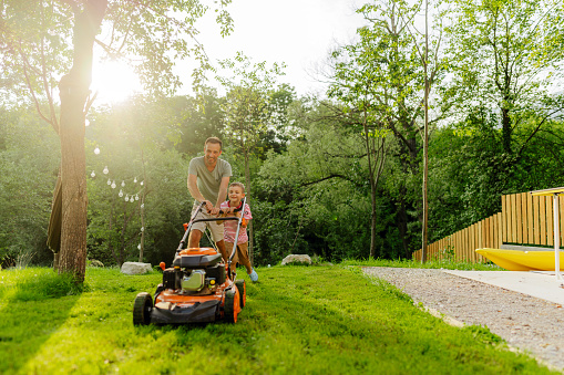 Photo of a young boy helping his father at mowing the lawn in their backyard