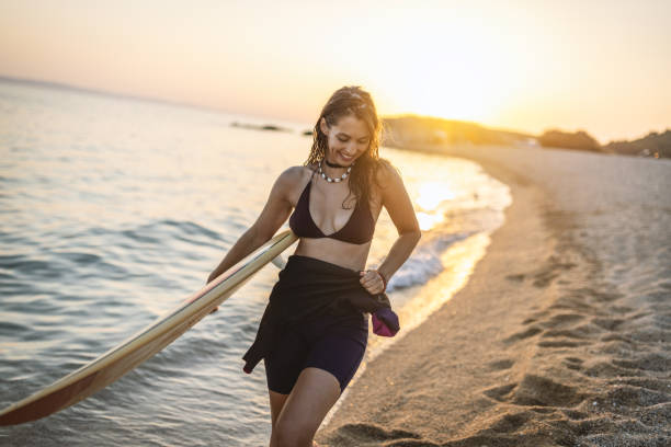 Beautiful surfer girl walking on the beach with surfboard at sunset