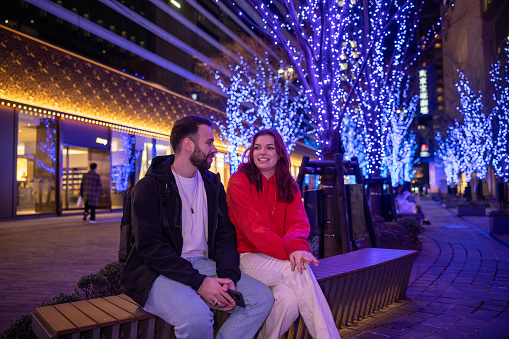 Young tourists sitting on bench under Christmas lights
