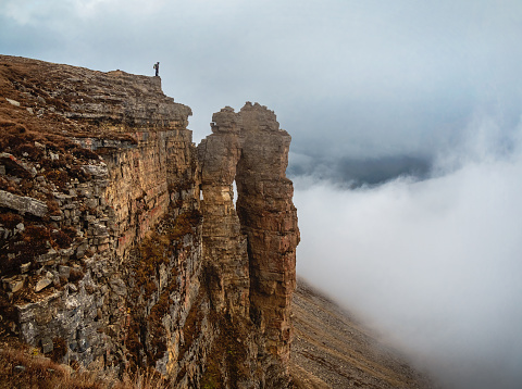 Soft focus. Tourist (man) stands on the cliff edge of Bermamyt plateau on high altitude under cloudy sky in foggy day. Rocks of Big Bermamyt - the so-called 