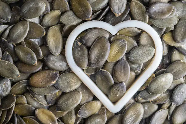 Photo of Green pumpkin seeds together with a heart shape as pattern background