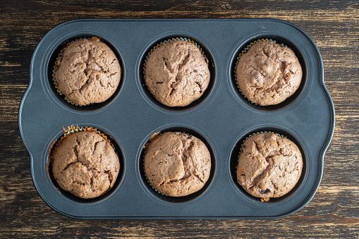 Six chocolate muffins in baking tray, top view