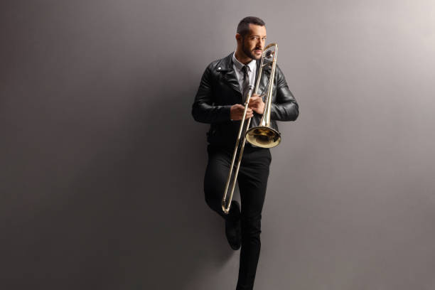 istock Young man with a trombone standing and leaning on a wall 1458145398