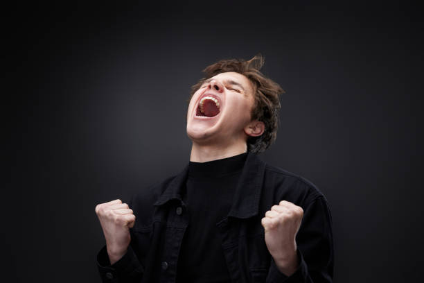 Portrait of excited man shouting and gesturing while standing against black background.