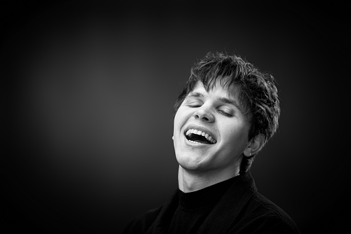 positive handsome man laughing on black background. black and white. copy space